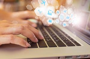 Fingers on laptop keyboard with white technology icons in upper right corner.